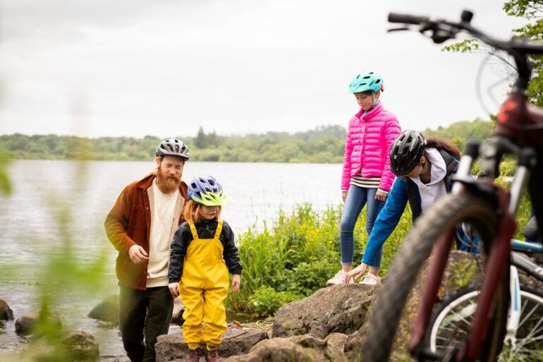 Two adults and two children wearing cycle helmets and standing on rocks.