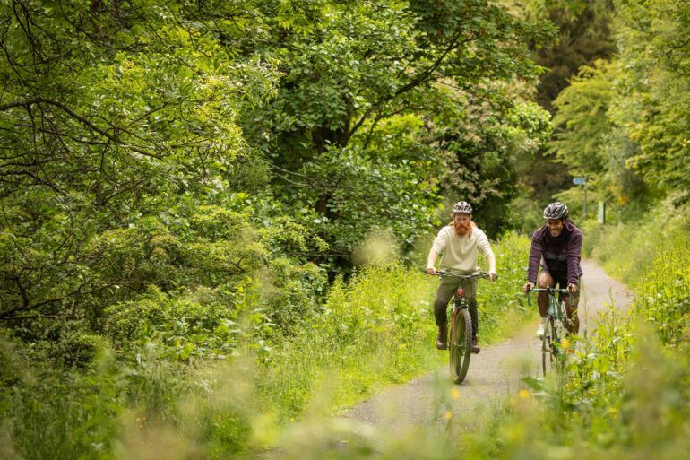 Two men cycling on woodland path.