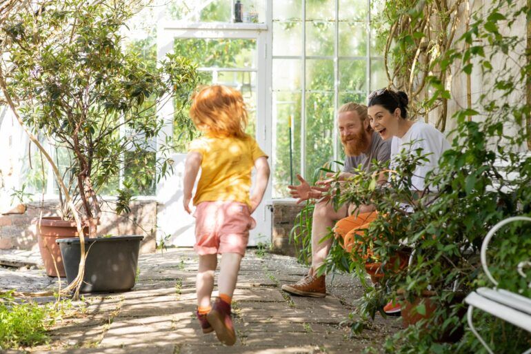 Woman and man sit on bench in greenhouse while child stands beside them