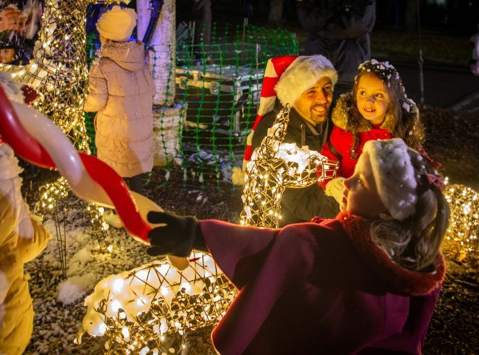 Man with Santa hat and young girl looking at gold Christmas fairy lights.